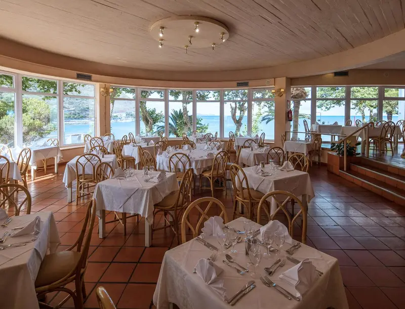 Une salle lumineuse avec des tables dressées face à une vue sur la mer.