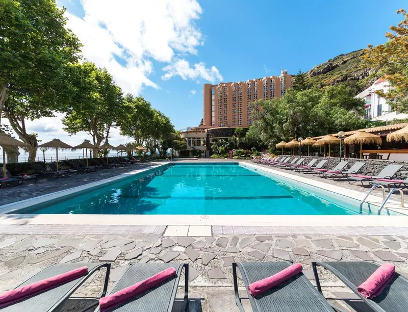 Une piscine rectangulaire bordée de transats roses et d'une végétation luxuriante.