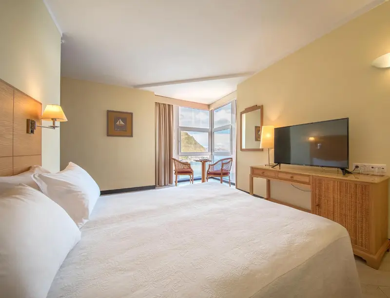 Chambre lumineuse avec un grand lit et une vue sur la mer.