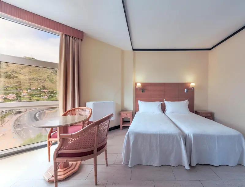 Chambre lumineuse avec un lit double et une vue sur un paysage montagneux.