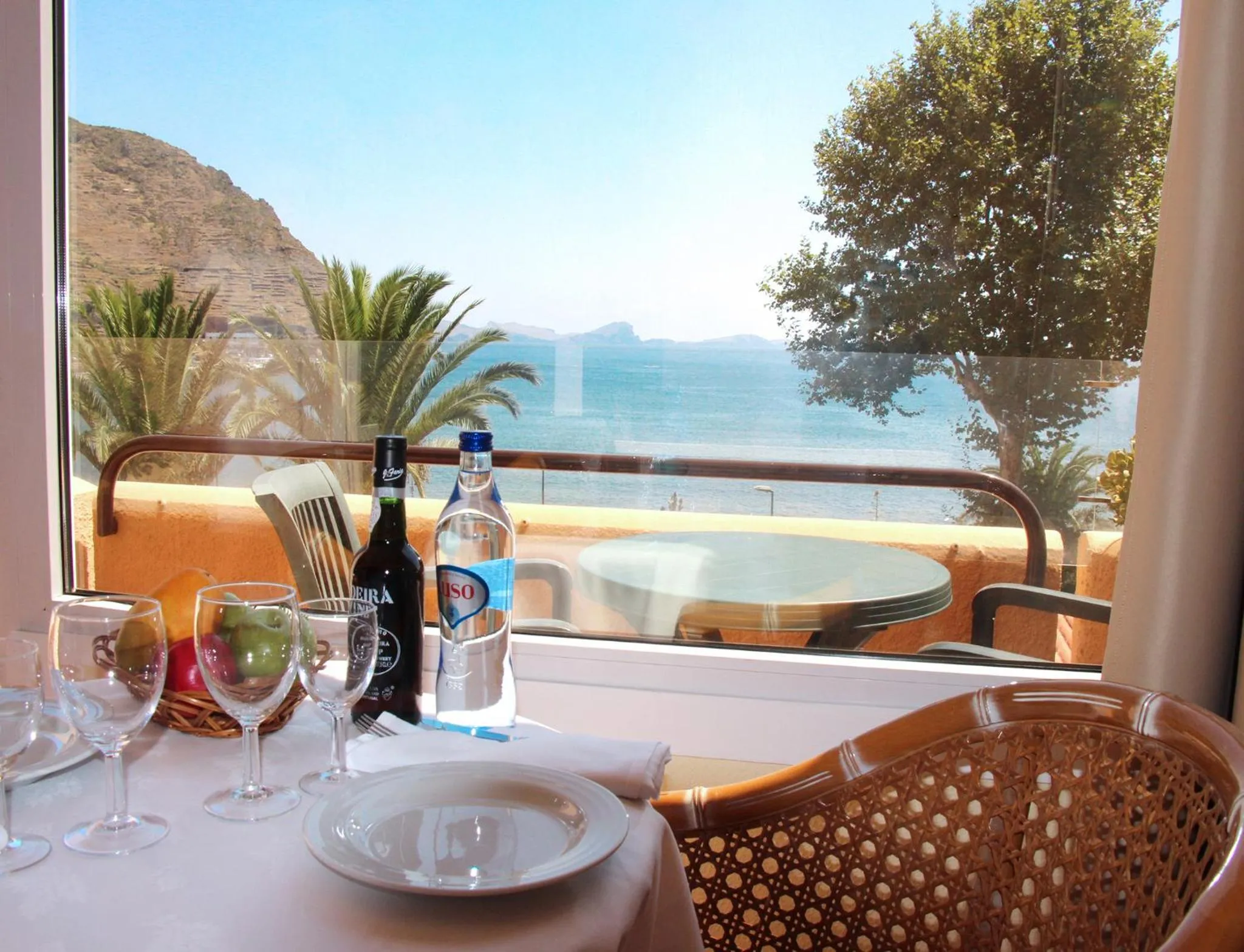 Une table est dressée avec des verres et des bouteilles devant une vue sur la mer.