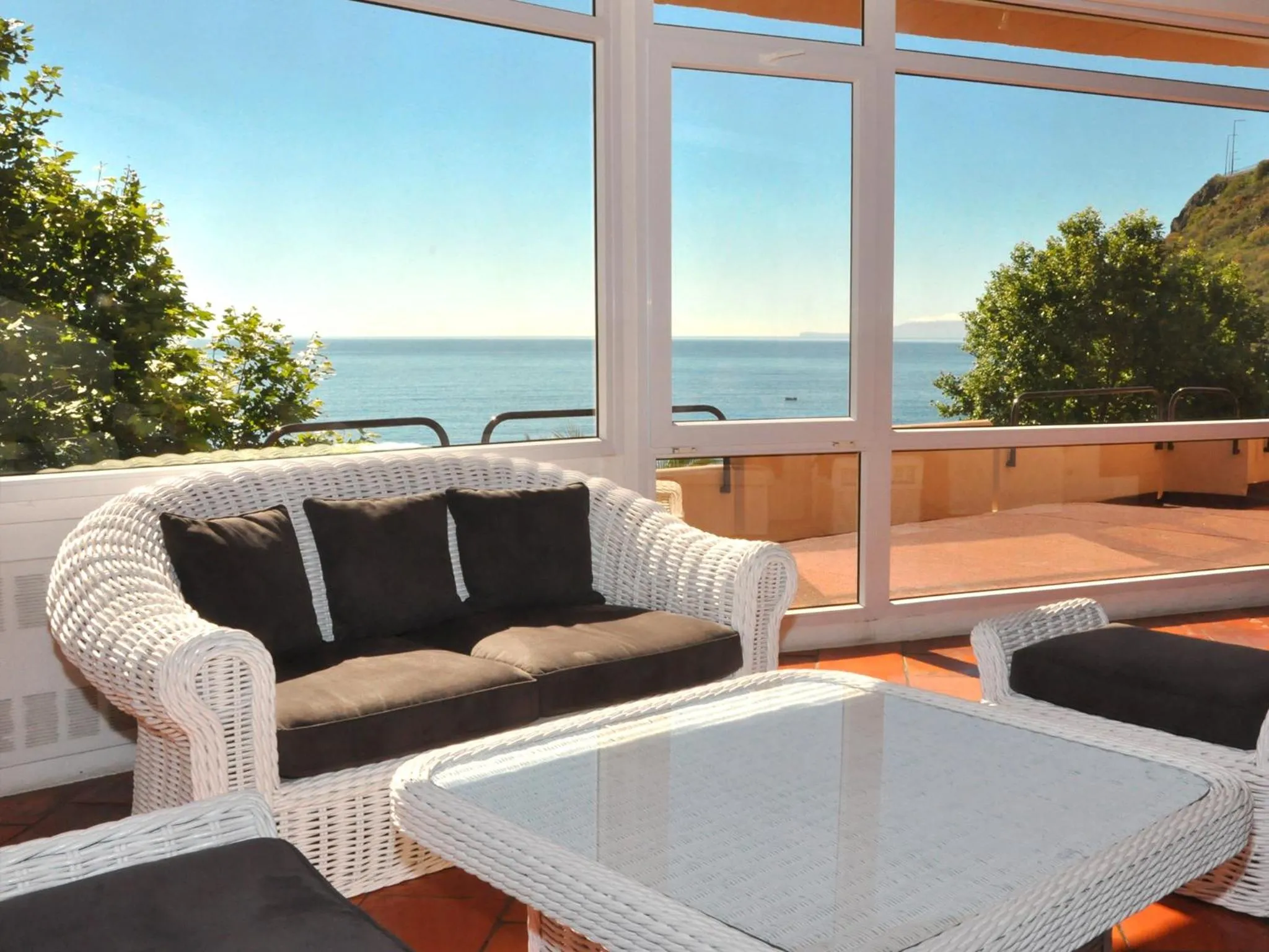 Canapé en rotin et table basse sur une terrasse avec vue sur la mer.