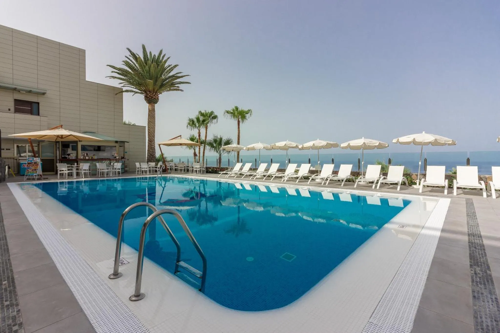 Piscine rectangulaire avec transats et parasols, vue sur la mer.