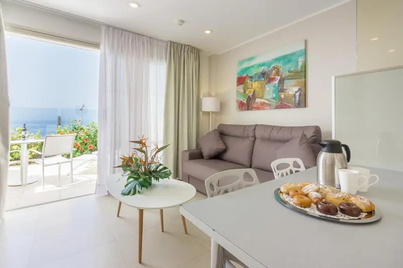 Espace de vie lumineux avec canapé, table basse et vue sur la mer.