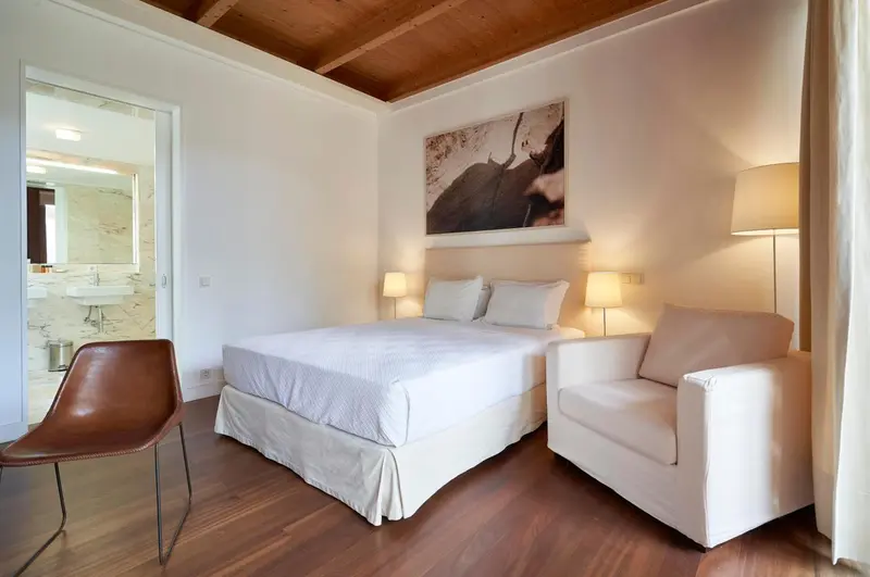 Une chambre lumineuse avec un lit double et un fauteuil.