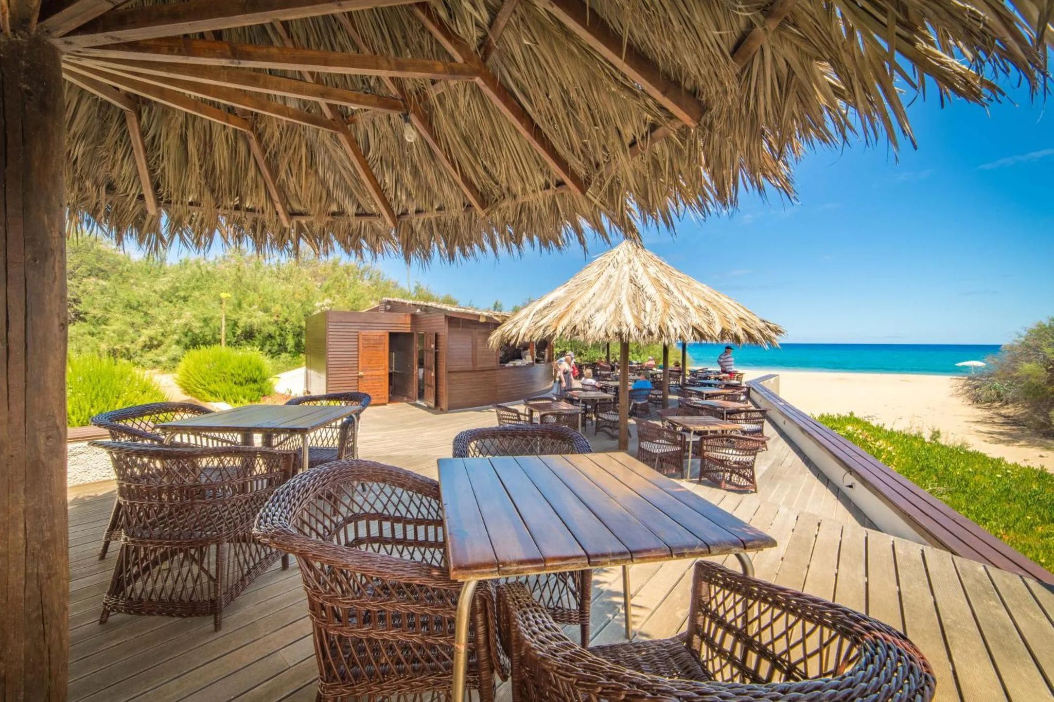 Terrasse ombragée avec tables et chaises en osier donnant sur la mer.