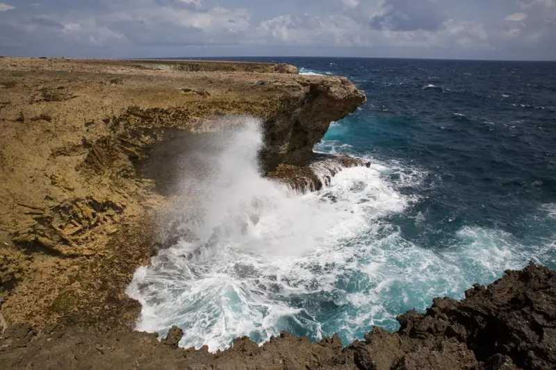 Vagues s'écrasant contre une côte rocheuse escarpée sous un ciel nuageux.
