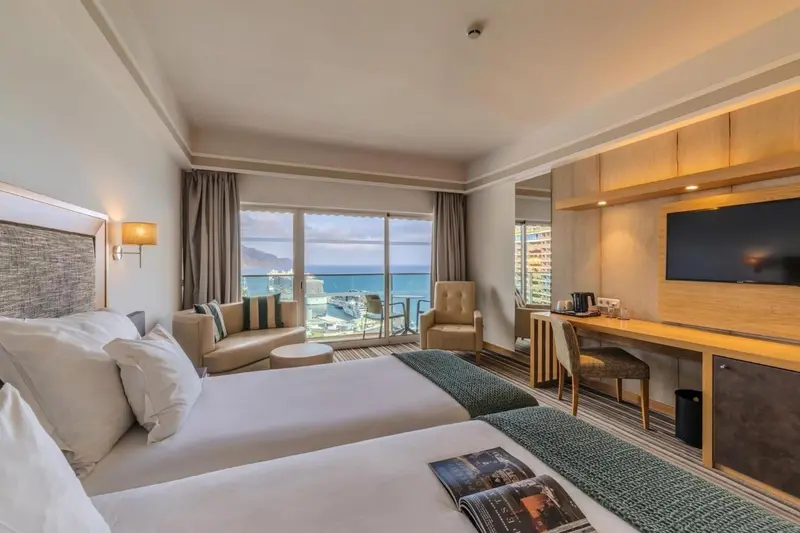 Chambre lumineuse avec un grand lit et une vue sur la mer.