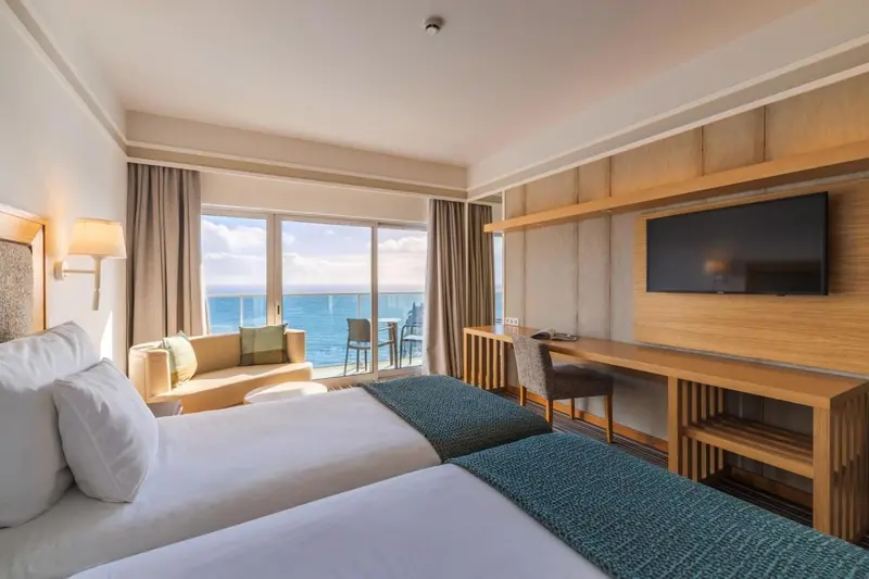 Chambre lumineuse avec un grand lit et une vue sur la mer.