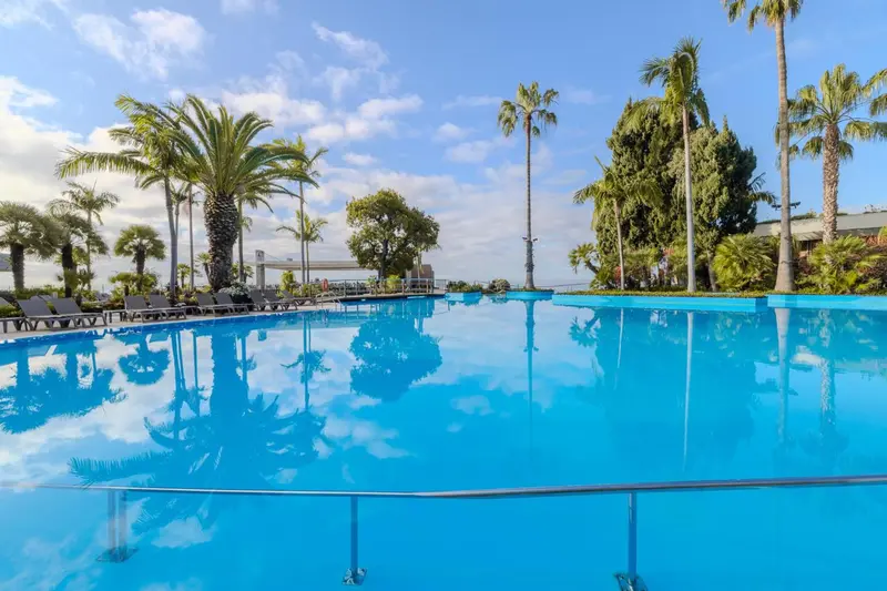 Une piscine rectangulaire turquoise reflète les palmiers et le ciel bleu.