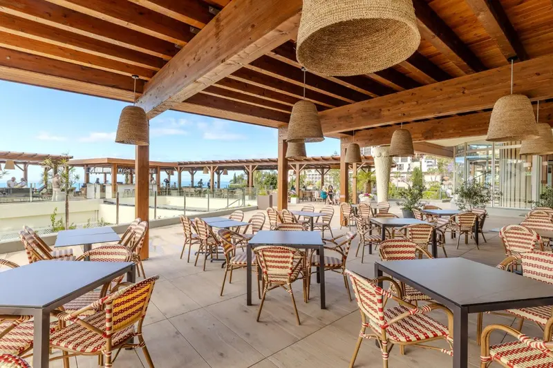 Terrasse ombragée avec tables et chaises donnant sur la mer.
