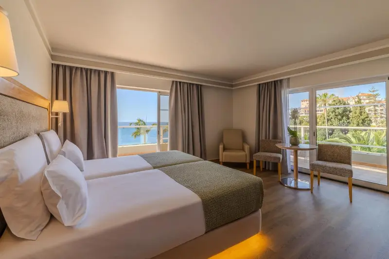 Une chambre lumineuse avec un lit double et un coin salon donnant sur une vue mer.