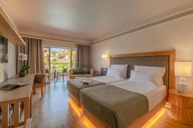 Chambre lumineuse avec deux lits simples et un coin salon près d'une fenêtre.