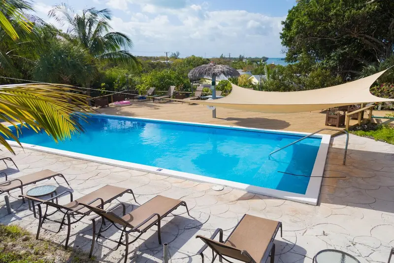 Une piscine rectangulaire bordée de chaises longues sous un abri ombragé.