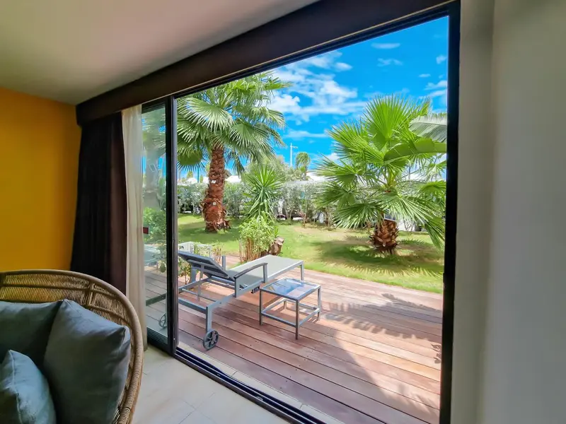 Vue sur une terrasse en bois avec des transats et des palmiers.