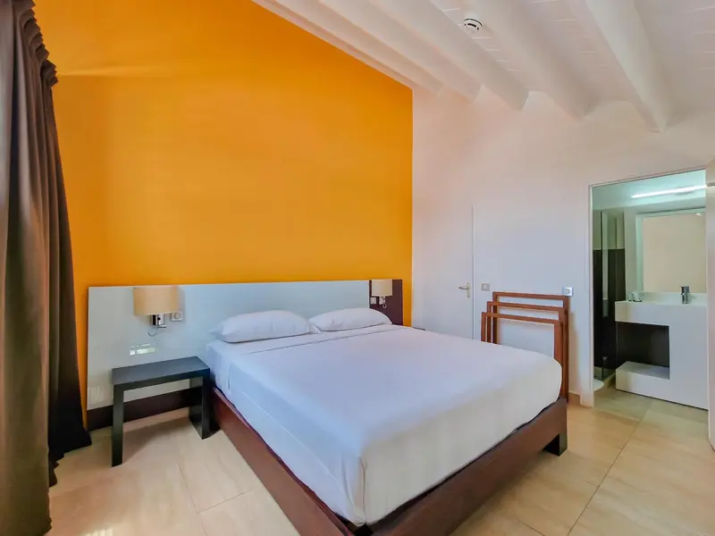 Une chambre lumineuse avec un grand lit et un mur orange vif.