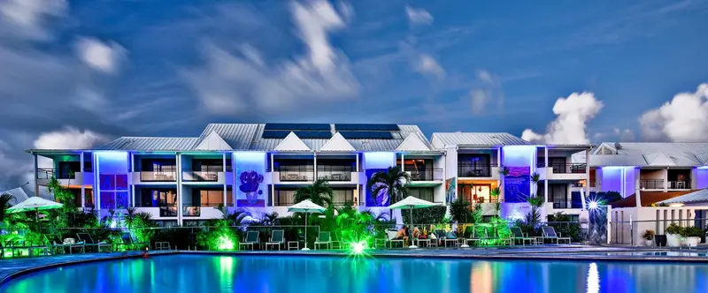 Bâtiment illuminé avec piscine au premier plan et végétation tropicale.