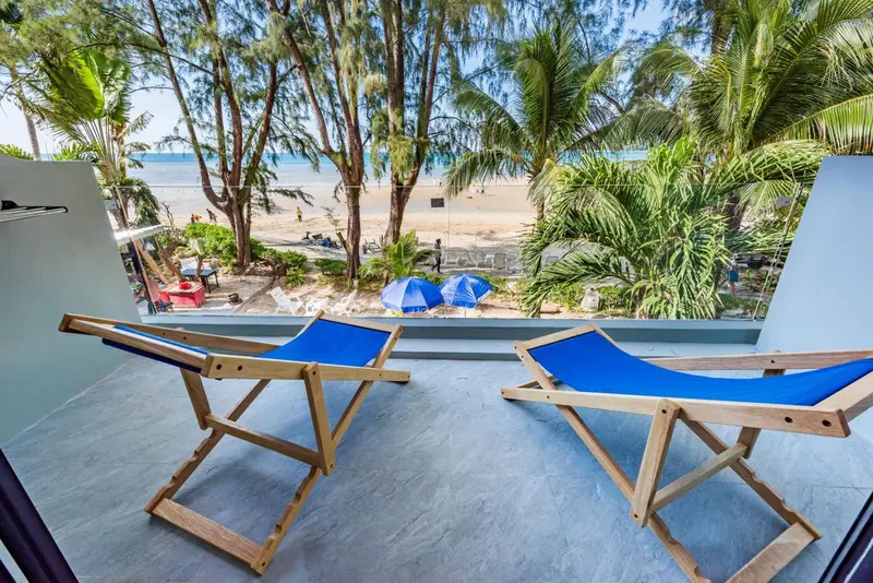 Deux transats bleus sur une terrasse donnant sur une plage de sable blanc et la mer.