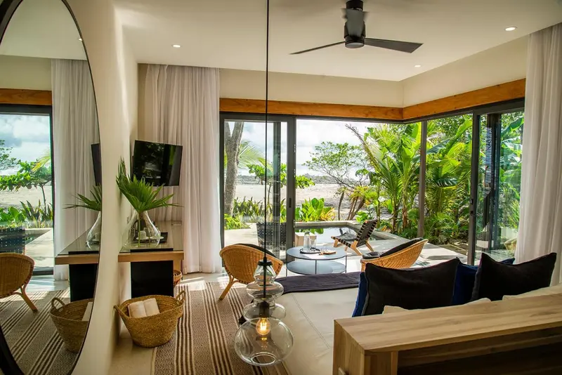 Espace de vie lumineux avec canapés et vue sur la végétation tropicale.