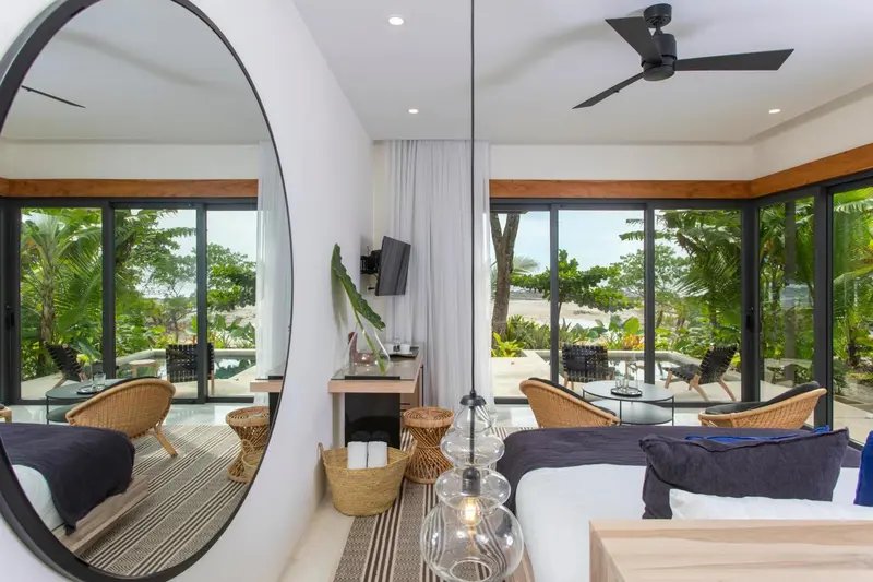 Une chambre lumineuse avec un grand miroir rond et une vue sur la végétation tropicale.