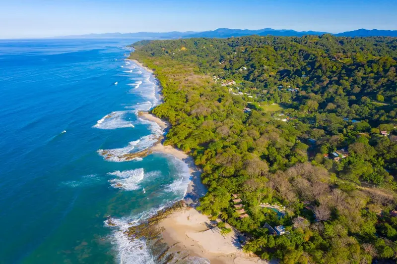 Vue aérienne d'une côte rocheuse bordée de végétation luxuriante et d'une plage de sable.