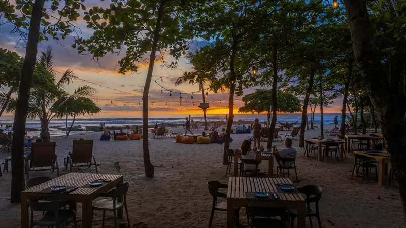Tables et chaises disposées sur le sable au coucher du soleil.