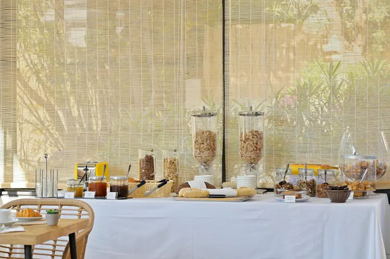 Un buffet propose des céréales, des viennoiseries et des confitures sur une table recouverte d'une nappe blanche.