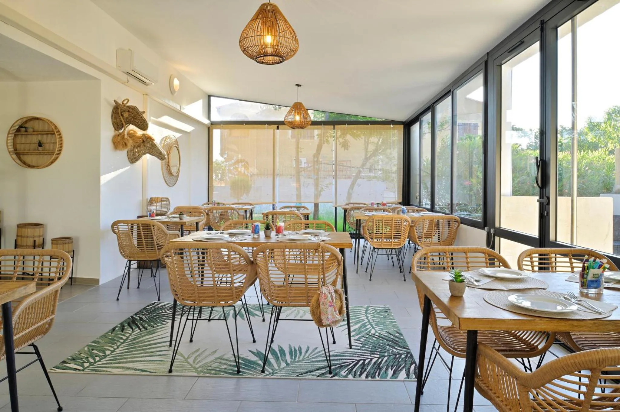 Une salle lumineuse avec des tables et des chaises en rotin est décorée de plantes et d'objets tressés.