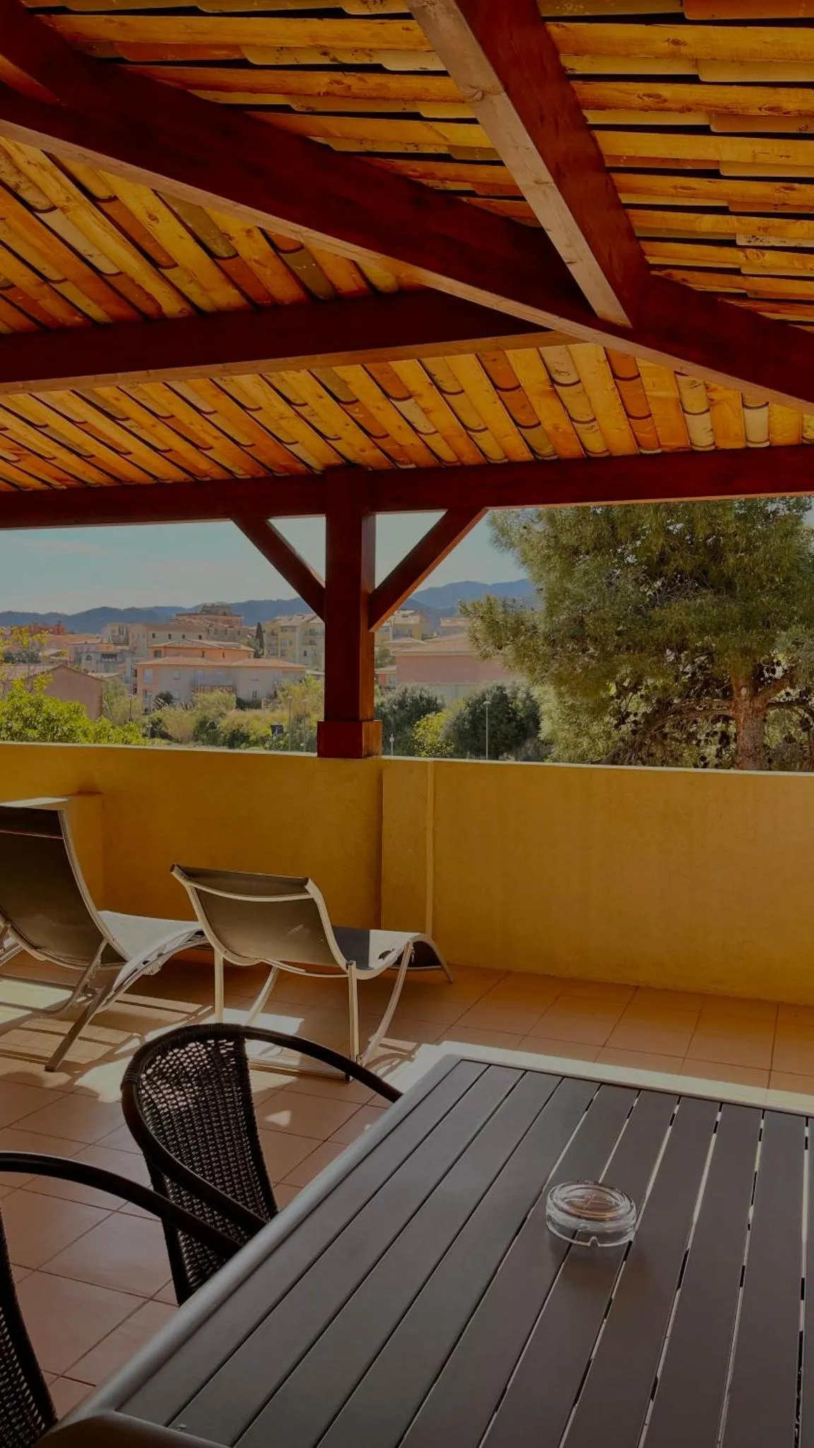 Terrasse ombragée avec mobilier de jardin et vue sur la ville.