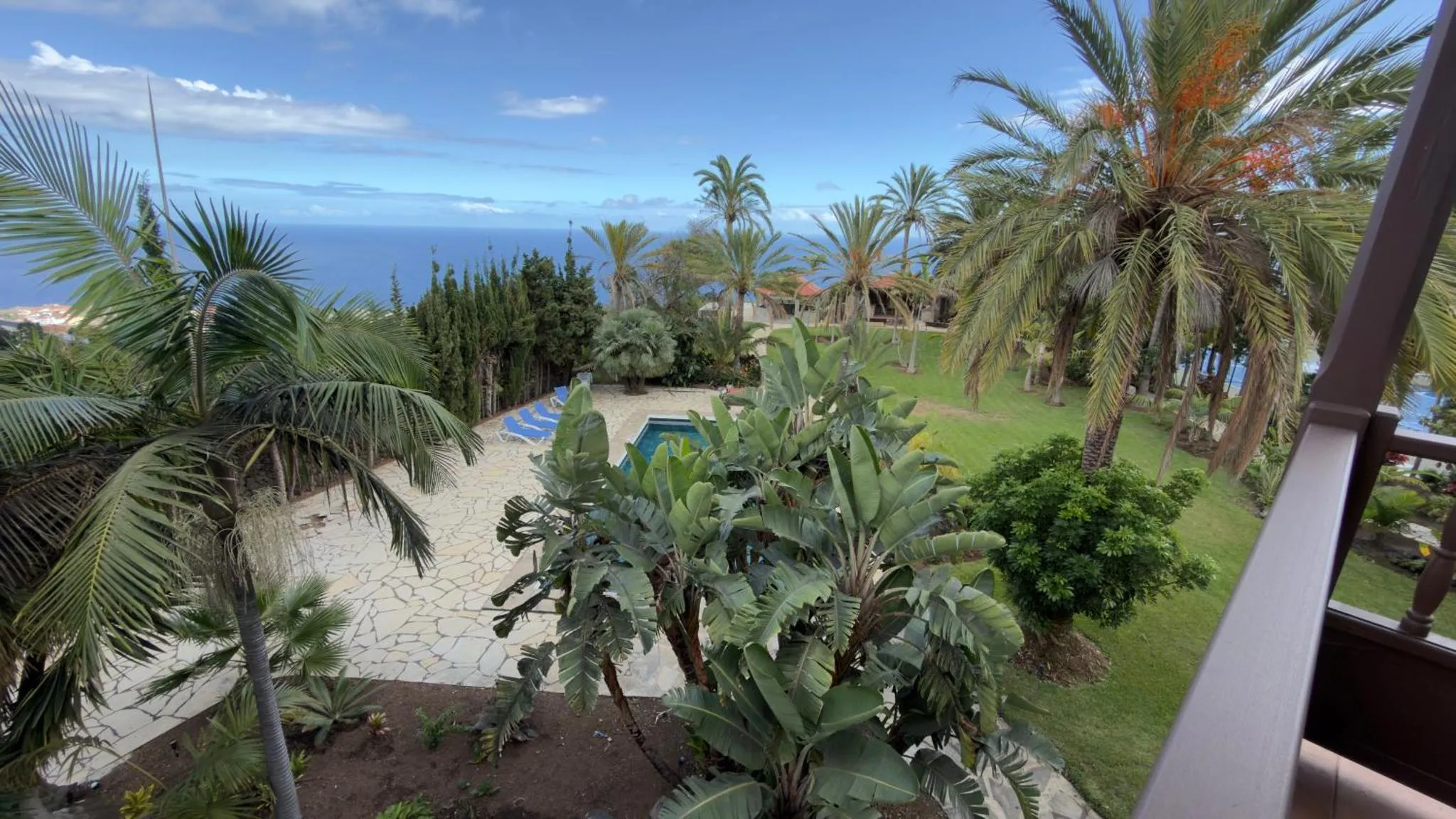 Vue d'un jardin tropical avec piscine et végétation luxuriante, surplombant la mer.