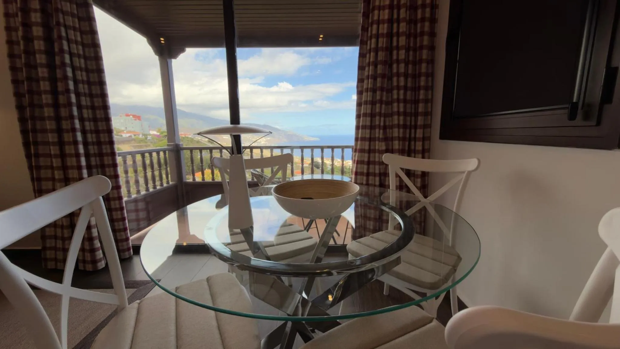 Table ronde en verre et chaises sur une terrasse avec vue sur la mer et les montagnes.