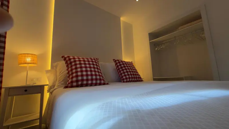 Une chambre lumineuse avec un lit recouvert d'une courtepointe blanche et de coussins à carreaux rouges.