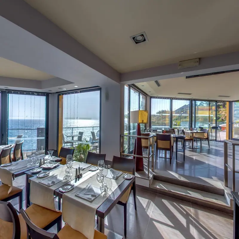 Une salle lumineuse avec des tables dressées face à une vue sur la mer.