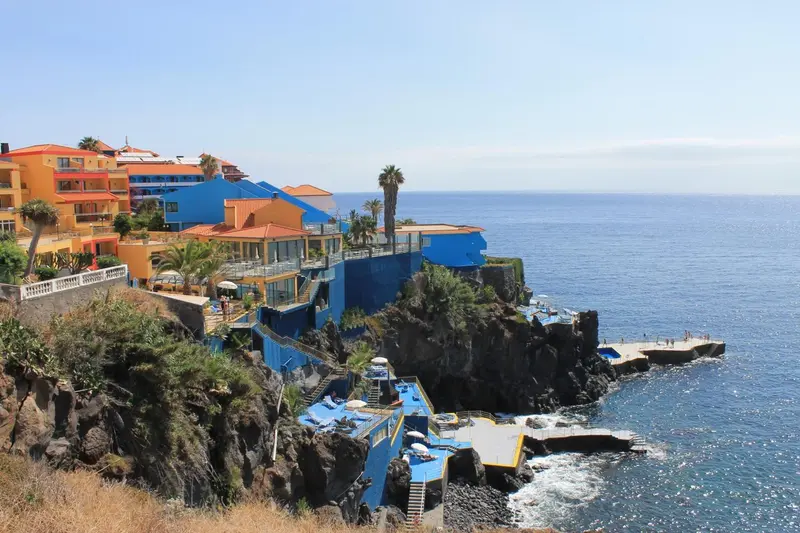 Vue d'un complexe hôtelier coloré surplombant une piscine naturelle rocheuse et l'océan.