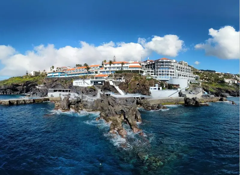 Vue aérienne d'un complexe hôtelier blanc surplombant une côte rocheuse et la mer.