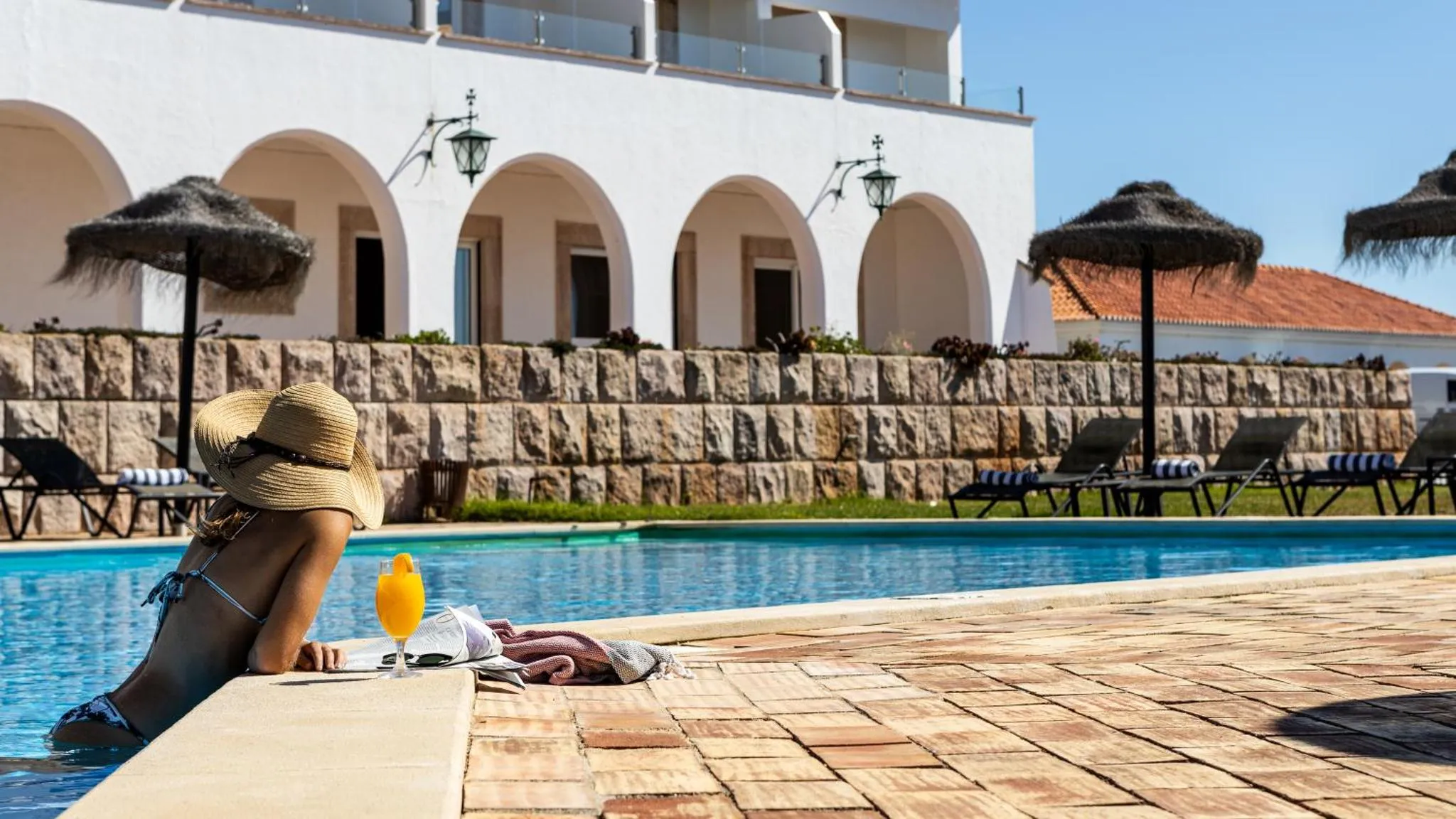 Une personne se détend au bord d'une piscine ensoleillée avec une boisson.