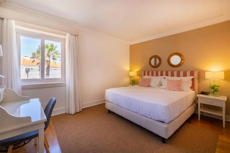 Chambre lumineuse avec un grand lit et une fenêtre donnant sur un paysage tropical.