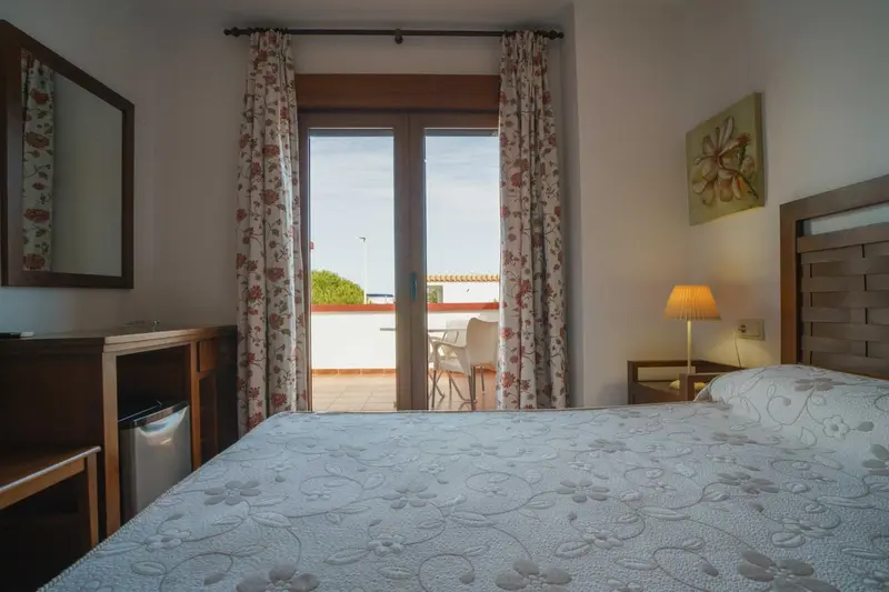 Une chambre lumineuse avec un lit recouvert d'une courtepointe et un accès à une terrasse.