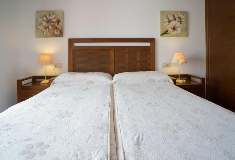Une chambre avec un grand lit recouvert d'une courtepointe blanche et deux tableaux floraux.