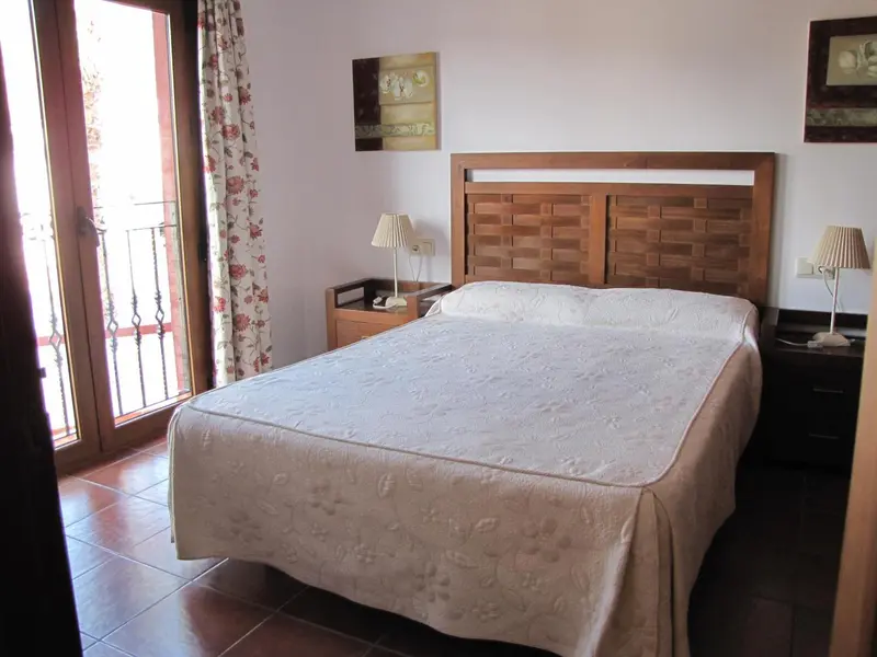 Une chambre lumineuse avec un grand lit et une porte-fenêtre donnant sur un balcon.