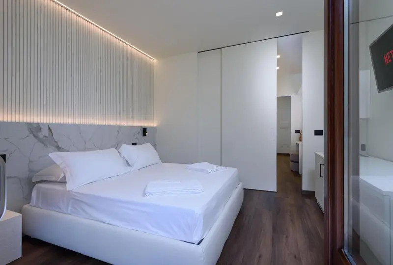 Une chambre lumineuse avec un grand lit blanc et un mur texturé.