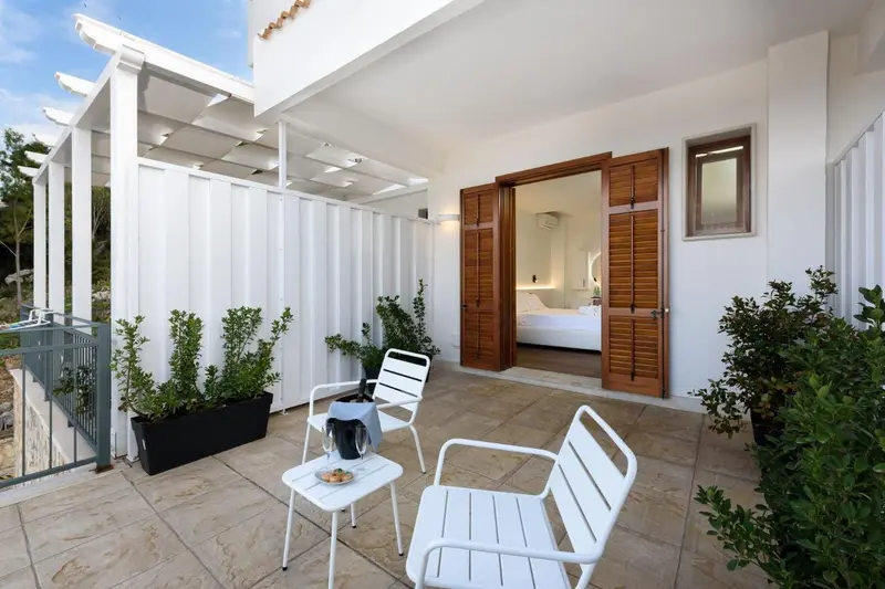 Terrasse carrelée avec mobilier blanc devant une ouverture sur une chambre.