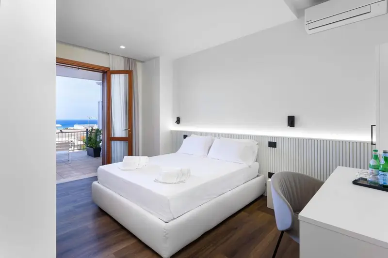 Une chambre lumineuse avec un grand lit et un balcon donnant sur la mer.
