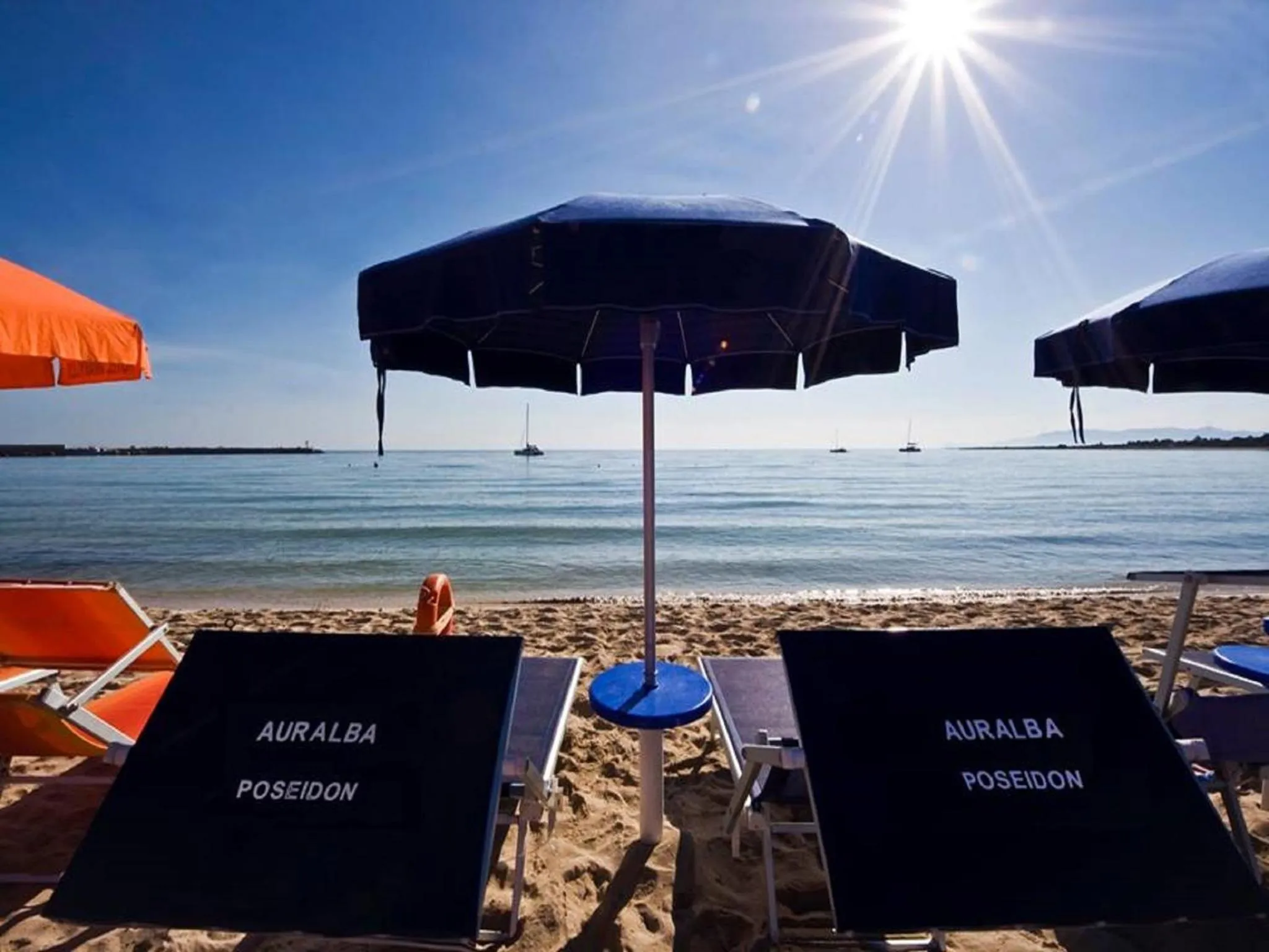 Transats noirs et parasols sur une plage de sable fin face à la mer.