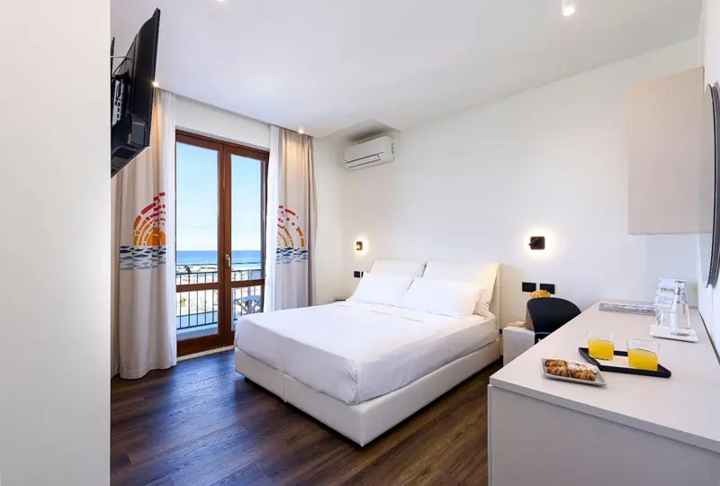 Chambre lumineuse avec un grand lit et vue sur la mer.
