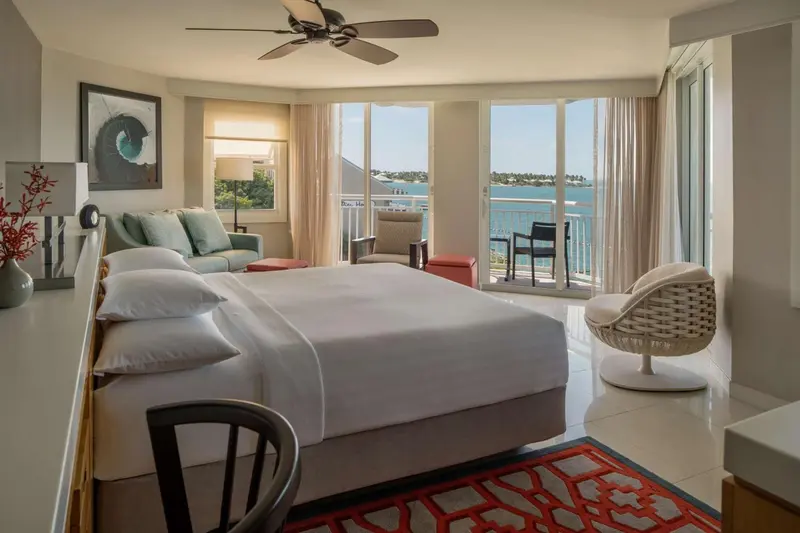 Une chambre lumineuse avec un grand lit et un accès à un balcon avec vue sur la mer.