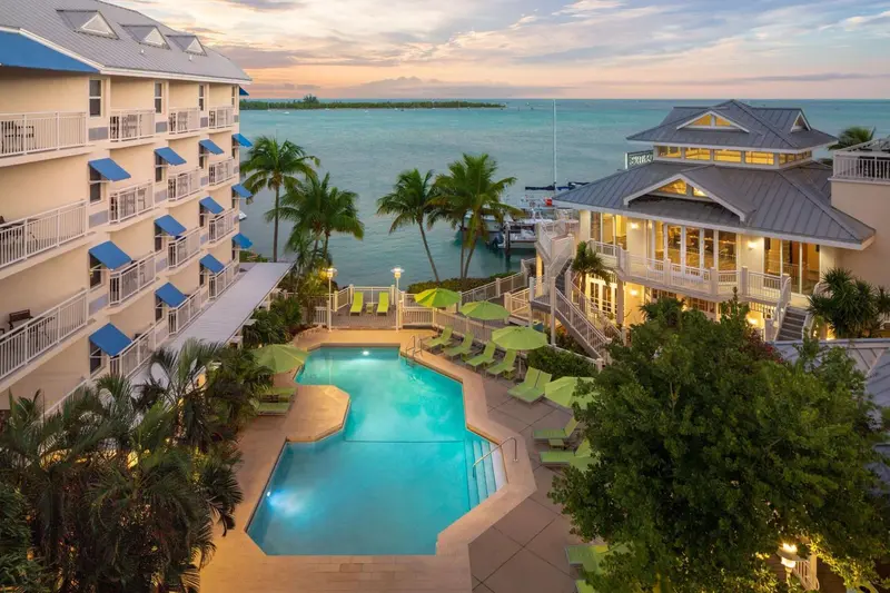 Vue aérienne d'un complexe hôtelier avec piscine et végétation tropicale au coucher du soleil.