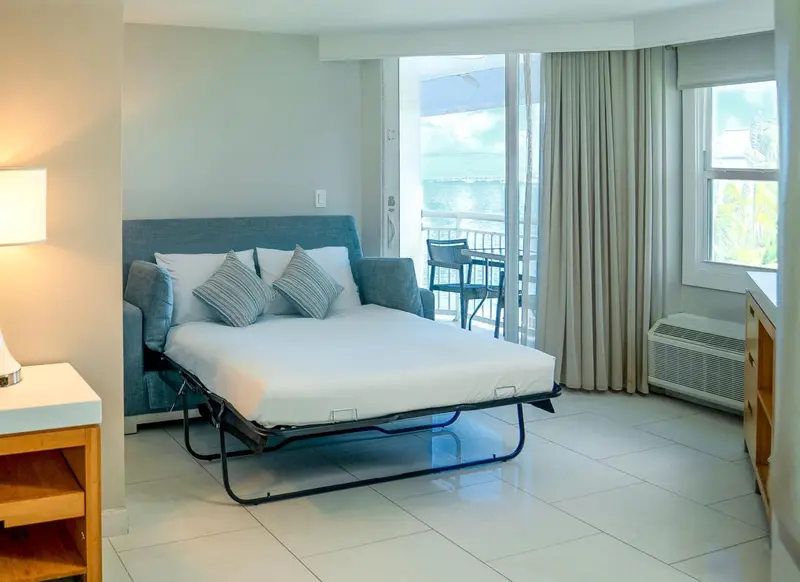 Chambre lumineuse avec un lit fait et un balcon ensoleillé.