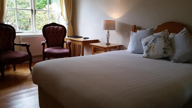 Une chambre lumineuse avec un lit fait et deux fauteuils.