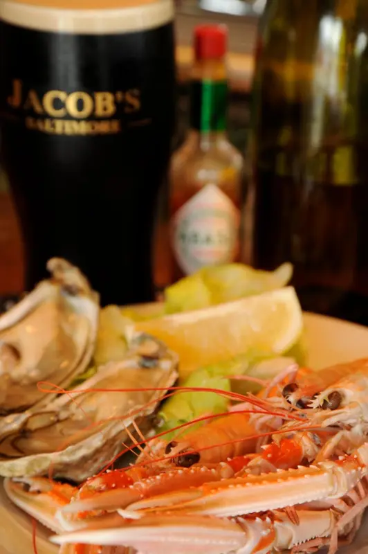 Une assiette de fruits de mer est présentée avec une bière et des sauces.